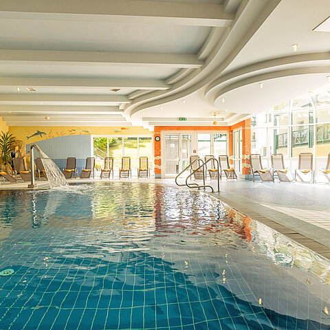 Innenpool mit Wasserfall und Liegestühlen in heller Spa-Landschaft