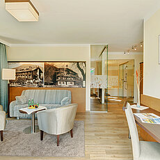 Helle Hotelsuite mit Sitzecke, Schreibtisch und offenem Badezimmer mit Glasdusche