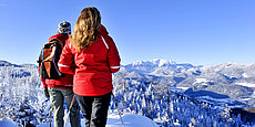 Zwei Wanderer in roten Jacken genießen winterliche Berglandschaft bei Sonnenschein