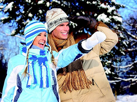 Happy couple in winter clothes pointing and smiling in snowy forest