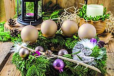 Adventskranz mit goldenen Kerzen, Tannenzweigen, Kugeln und rustikaler Holzdeko