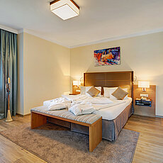 Modernes Hotelzimmer mit Doppelbett, Zierkissen, Bademänteln und warmer Beleuchtung