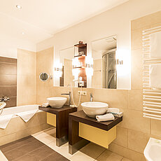 Modernes Hotelbad mit Doppelwaschbecken, Badewanne, Spiegeln und warmem Ambiente-Licht