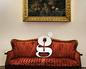 Vintage-Rot-Samtsofa mit weißem typografischem Buchstaben g vor gerahmtem Stillleben-Gemälde