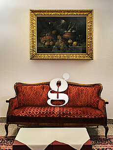 Vintage-Rot-Samtsofa mit weißem typografischem Buchstaben g vor gerahmtem Stillleben-Gemälde