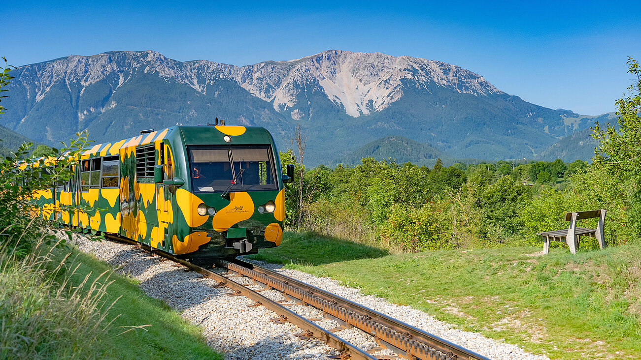 Bunter Touristenzug auf Bahngleis in den österreichischen Alpen unter klarem Himmel