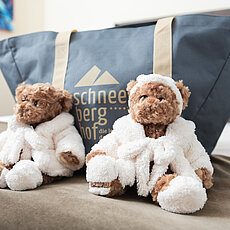 Zwei Plüsch-Teddybären in weißen Bademänteln vor einer Tasche vom Hotel Schneeberg Hof