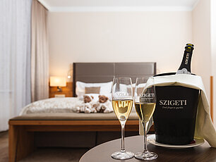 Two glasses of sparkling wine with Szigeti bottle in hotel room with double bed