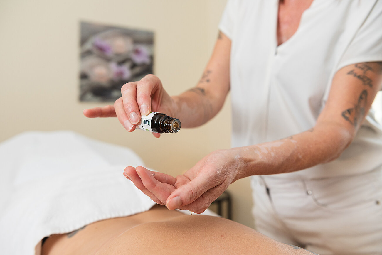 Masseurin trägt ätherisches Öl auf die Hände auf vor einer Rückenmassage