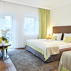 Modernes Hotelzimmer mit Doppelbett, grünen Vorhängen, Sesseln und Orchidee auf dem Tisch