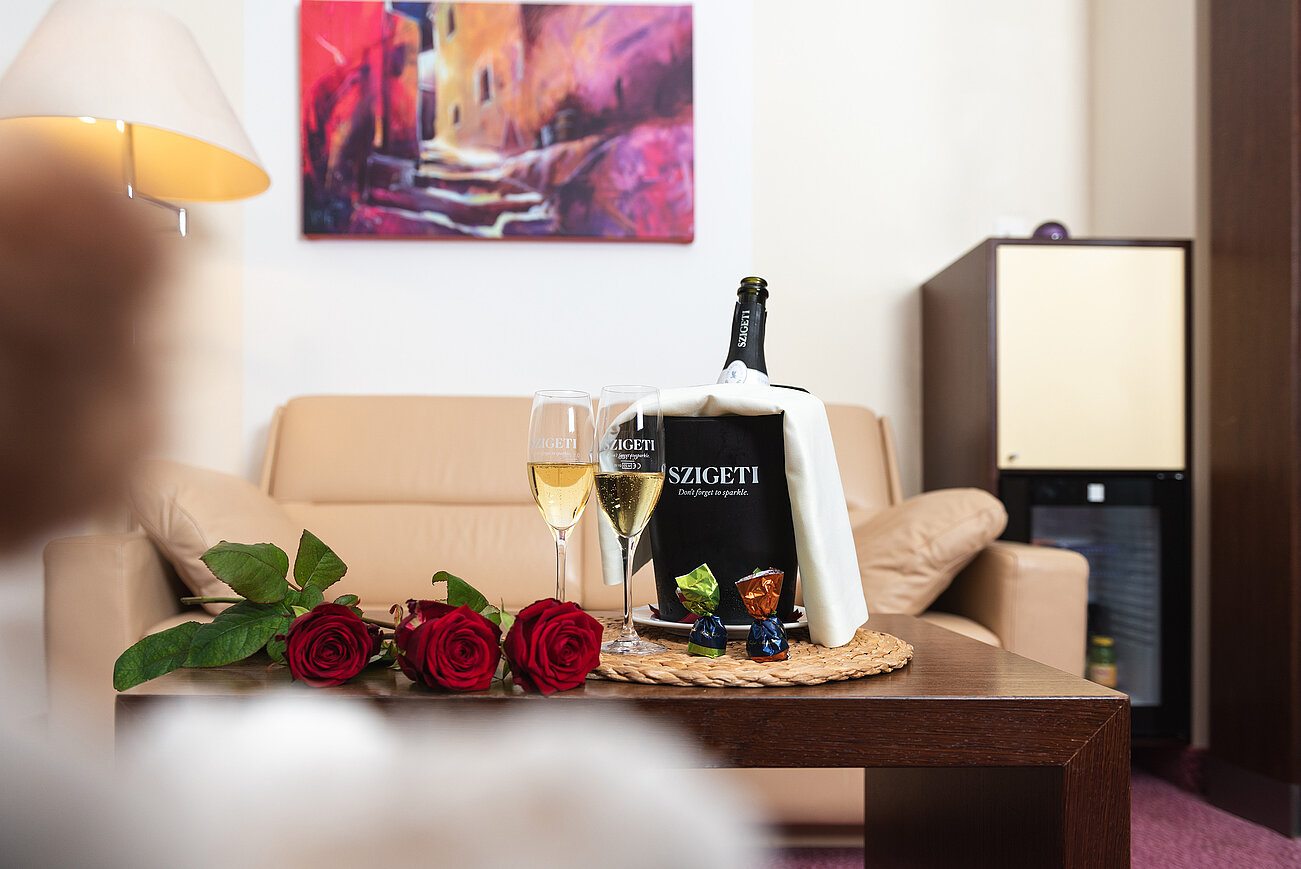 Romantisches Hotelzimmer mit Szigeti-Champagner, roten Rosen und Pralinen auf dem Couchtisch