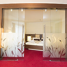 Moderne Hotelsuite mit roten Teppichboden, Doppeltür aus Milchglas und Doppelbett