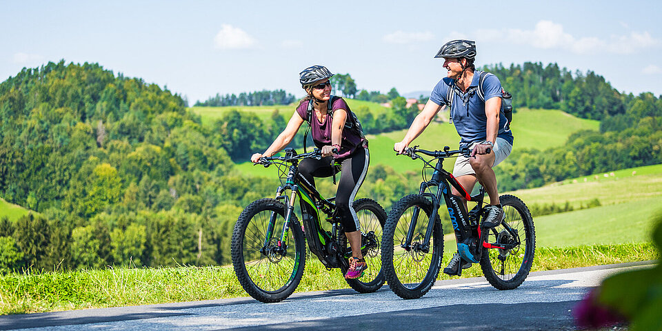 Paar fährt E-Mountainbikes durch die idyllische Landschaft an einem sonnigen Tag