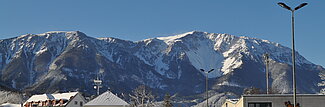 Verschneite Stadtstraße mit Winterpanorama der Berge unter klarem blauen Himmel