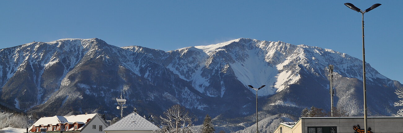 Verschneite Stadtstraße mit Winterpanorama der Berge unter klarem blauen Himmel