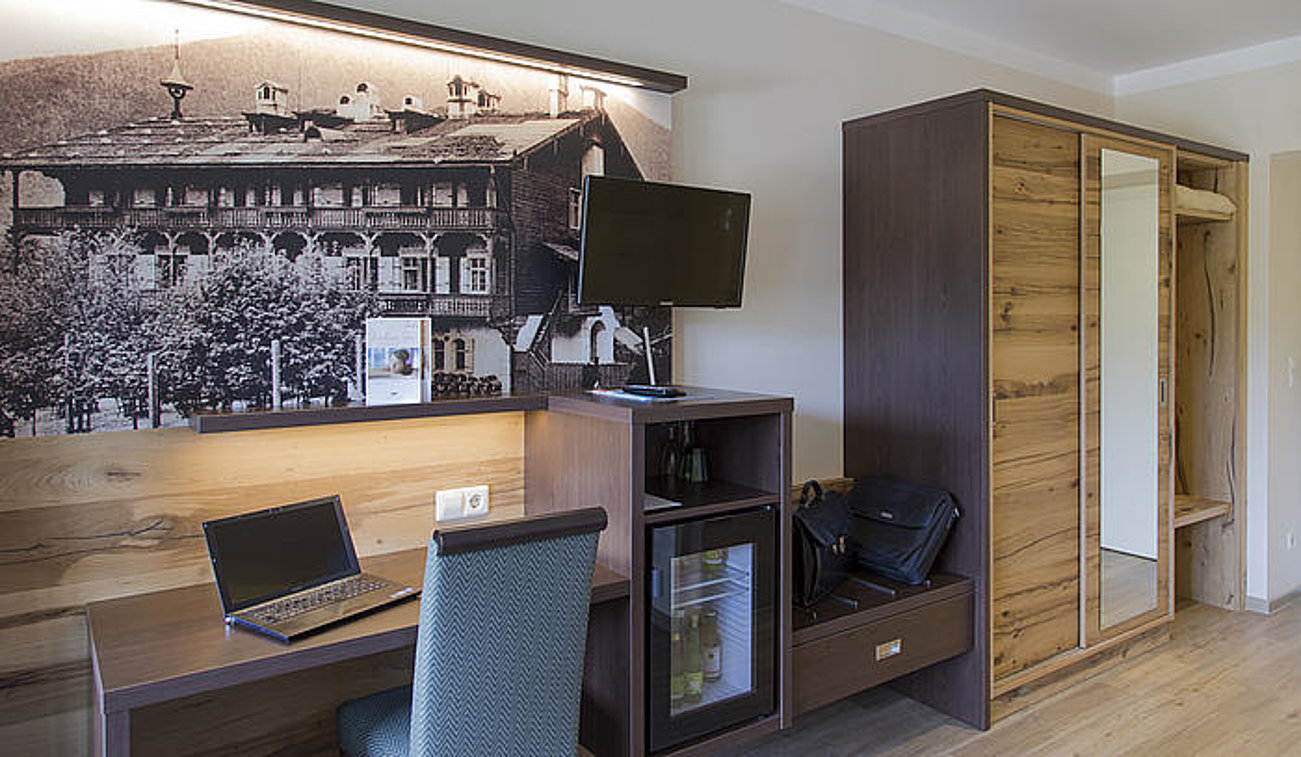 Modern hotel room workspace with laptop, wall-mounted TV, and wooden wardrobe