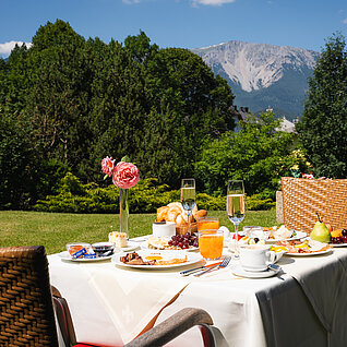 Frühstückstisch im Freien mit Bergblick, frischem Gebäck, Obst und Getränken