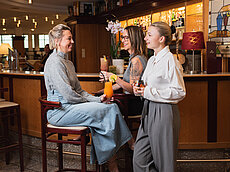 Drei Frauen unterhalten sich mit Cocktails an einer stilvollen Bar mit warmer Beleuchtung