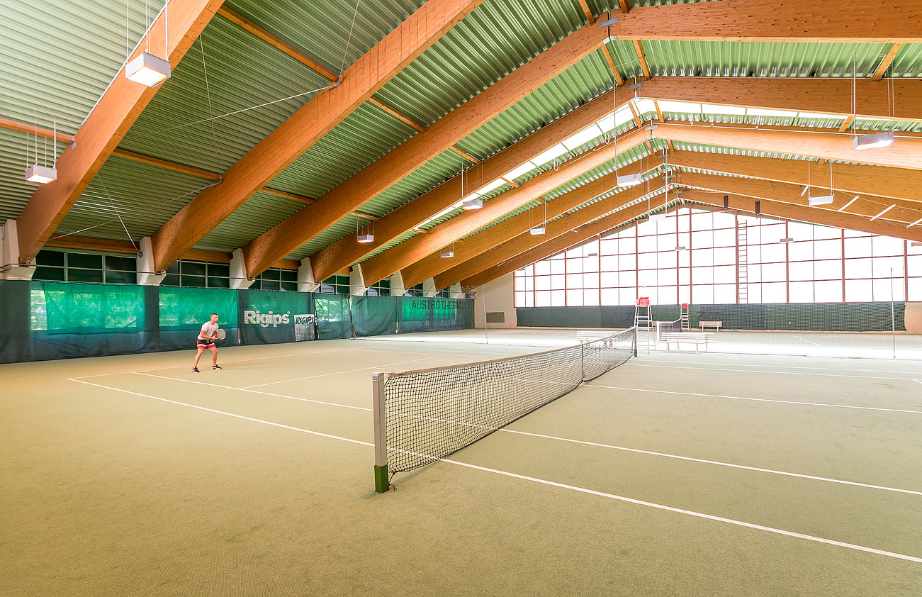 Tennisspieler auf Indoorplatz mit Holzdecke bereit zum Aufschlag