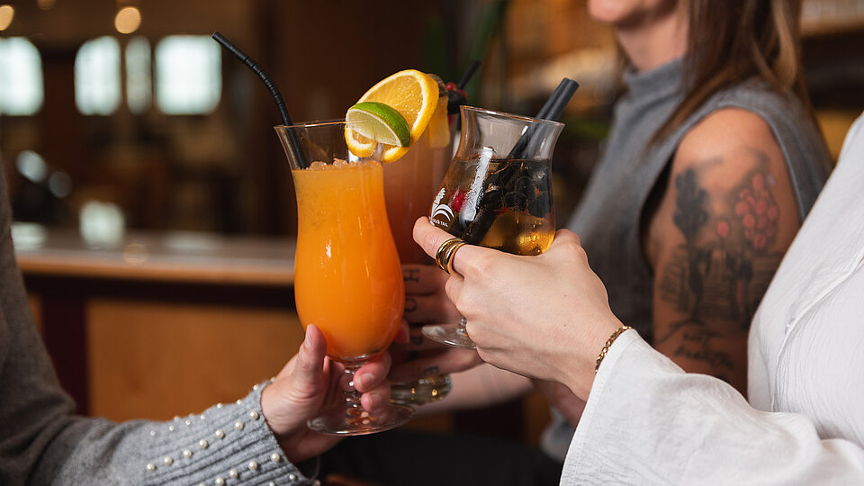 Freunde stoßen mit bunten Cocktails an einer Bar mit Garnitur und Strohhalmen an