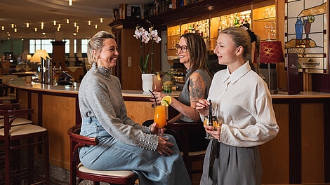 Drei Frauen genießen Cocktails und Unterhaltung an einer stilvollen Hotelbar