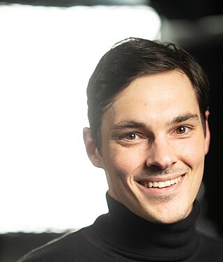 Lächelnder Mann im schwarzen Rollkragenpullover im Studio mit weicher Beleuchtung