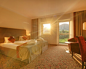 Cozy hotel room with double bed, red decor, and mountain view during sunset