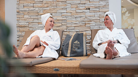 Zwei Frauen in Bademänteln entspannen auf Liegen im Wellnesshotel Schneeberghof