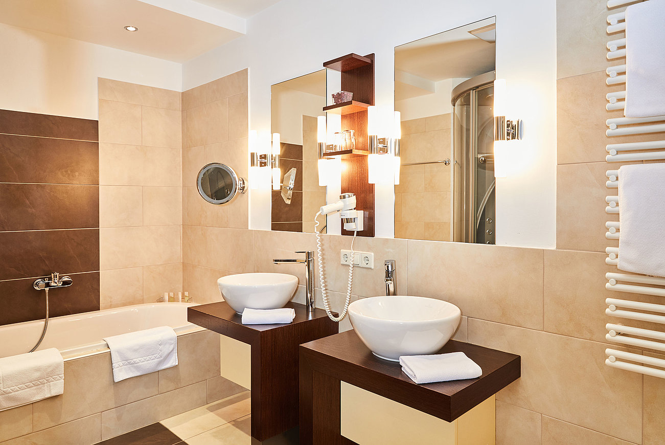 Modern hotel bathroom with double sink, bathtub, hairdryer, and warm lighting